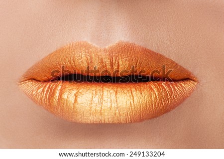 Cosmetics and make-up. Close-up shoot of a beautiful woman with golden lips lipstick and gloss. Golden creative lip gloss. Sweet kiss. Close-up of beautiful full lips girl. Beautiful skin.