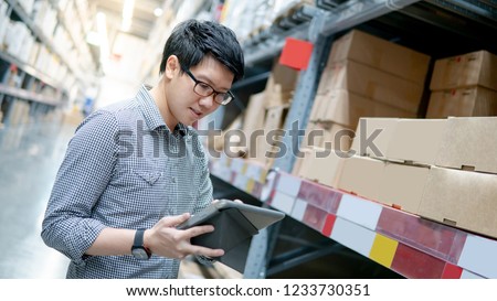 Asian manager man doing stocktaking of products in cardboard box on shelves in warehouse using digital tablet and pen. Male professional assistant checking stock in factory. Physical inventory count.