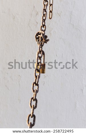rusty chain and lock  hanging in front on a white wall
