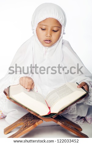 A muslim girl wearing praying attire reading the holy quran A muslim girl wearing praying attire reading the holy quran