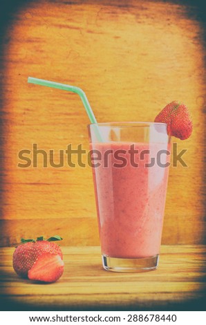 Milk shake with fresh berries and straw on wooden background with vintage tone