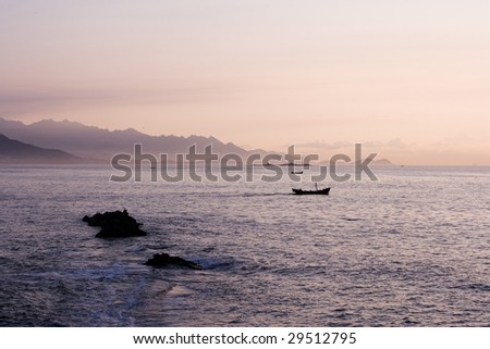 Early morning, calm sea and light red sky over maountains in background