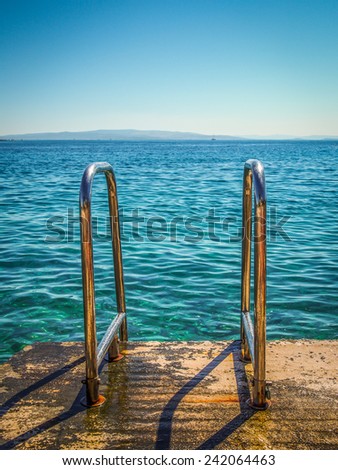 Metal railing descent to the sea. Blue sea and blue sky.