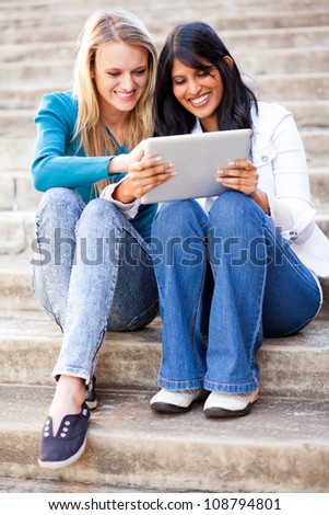 two young female college friends using tablet computer together outdoors