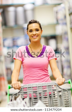 happy young woman pushing trolley in supermarket