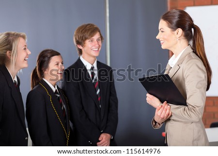 happy high school teacher talking to students in classroom