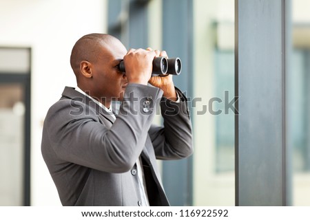 determined african american businessman using binoculars in office
