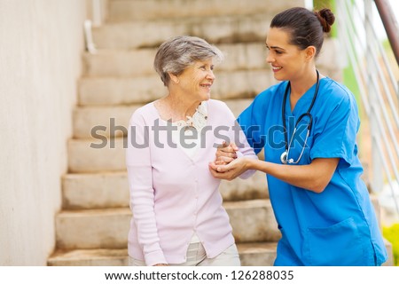 young caregiver helping senior woman walking down stairs