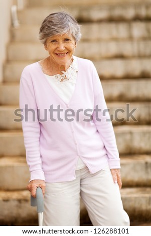 happy elderly lady standing by stairway with cane