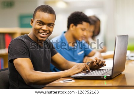 happy male african college student using laptop in library