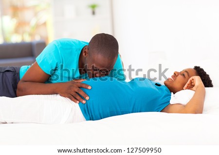 young african american man kissing pregnant wife\'s belly on bed