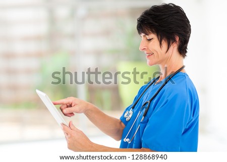 cute middle aged medical nurse using tablet computer in office
