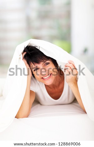 fun middle aged woman lying under duvet laughing