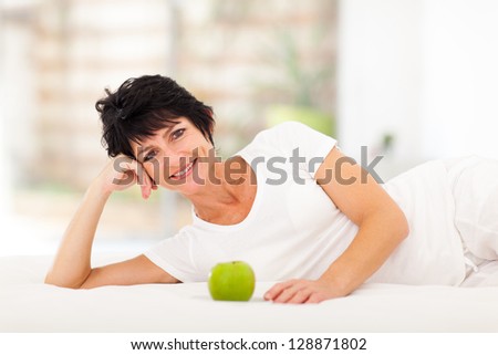 attractive mature woman lying on bed with a green apple in front