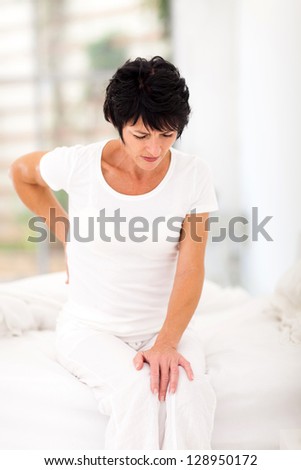 middle aged woman sitting on bed having back pain