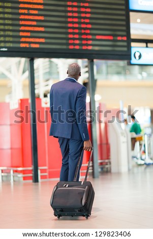 african businessman with luggage looking at flight information board in airport