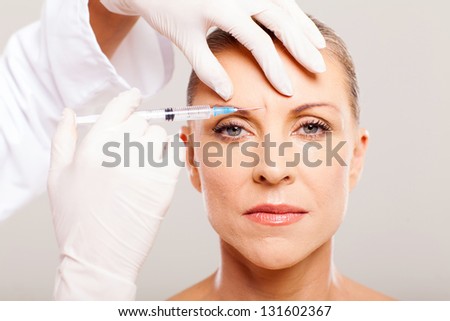 cosmetic surgeon giving face lifting injection to mature woman