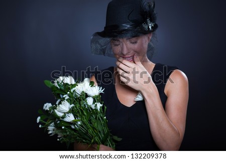 sad widow with mourning clothing and flowers crying at husband\'s funeral
