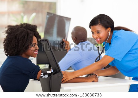 caring african young nurse checking patient\'s blood pressure in doctor\'s office