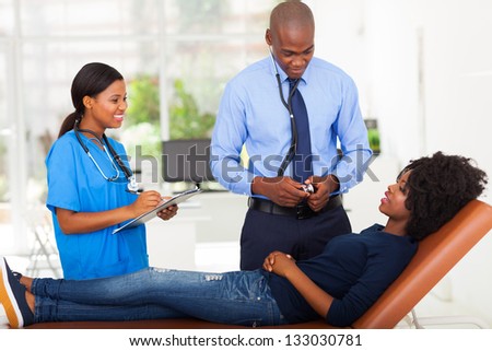 female African patient lying on doctor\'s examining couch and complaining to doctor about her sickness