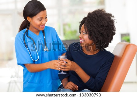 friendly african nurse giving patient glass of water in doctors office