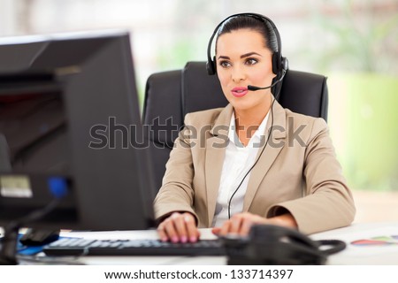 Beautiful young female call center operator with headset in office