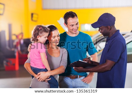 friendly auto mechanic talking to young family in garage