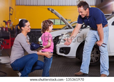 cute little girl hiding auto technician\'s hat in garage