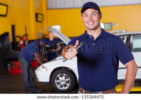 happy male auto mechanic giving thumb up holding wrench