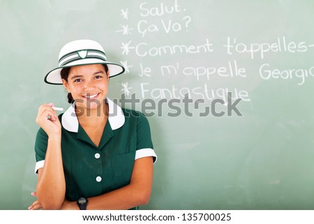 portrait of smiling french teen girl holding chalk in front of chalkboard in classroom