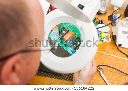 senior technician examining a computer board under electrical magnifying glass