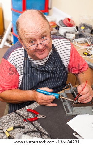 happy senior technician working with soldering iron in workshop