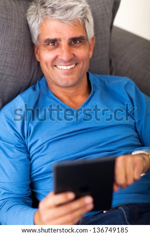 overhead portrait of mature man using tablet computer while lying on sofa