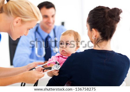pediatric nurse playing with baby girl while her mother talking to pediatrician