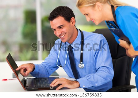 happy male doctor and medical assistant looking at computer