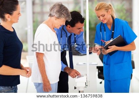 medical doctor monitoring senior patient\'s weight with his assistant