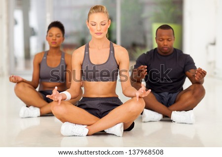 group of young fit people meditating in a gym class