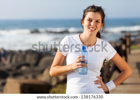 cute teen girl drinking water after morning workout at the beach