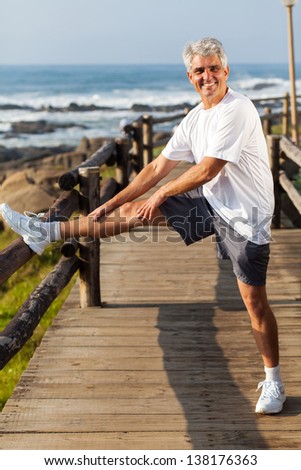 active mature man stretching leg at the beach in the morning