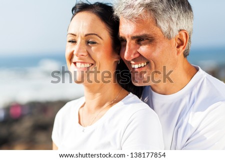 happy mid age husband and wife hugging at the beach