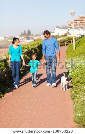 beautiful young couple with their daughter walking pet dog by seaside