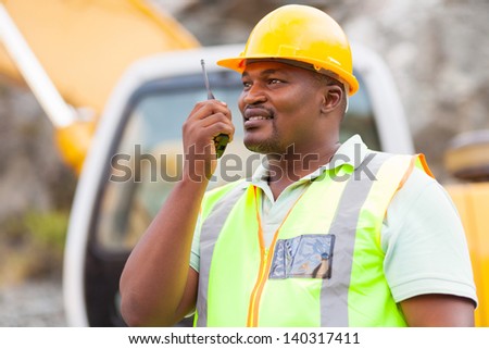 afro american industrial worker talking on walkie-talkie at mining site