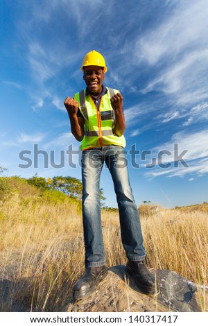 excited young construction worker on top of rock outdoors