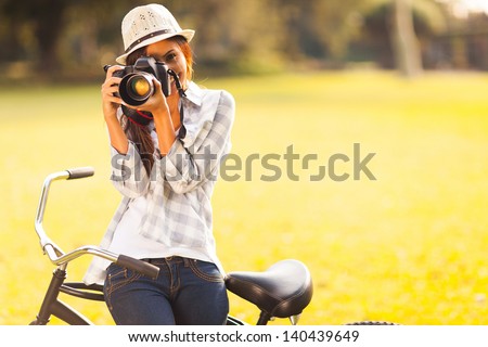 smiling young woman using a camera to take photo outdoors at the park