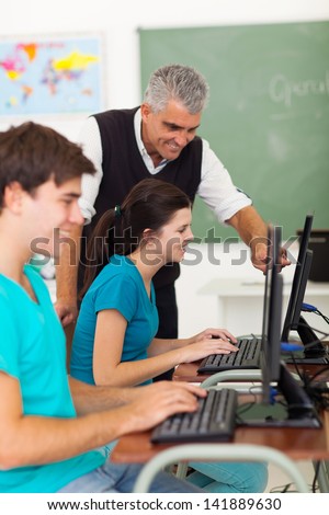 cheerful middle aged teacher helping high school students with computer work