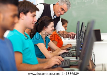 friendly middle aged teacher teaching computer to high school students