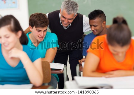friendly senior high school teacher helping students in classroom