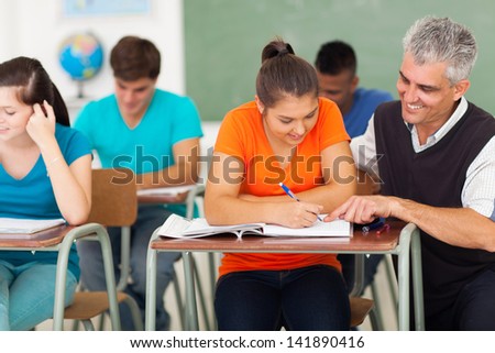 middle aged high school teacher helping a student in classroom
