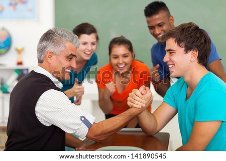 friendly middle aged teacher arm wrestling with high school student in classroom during break