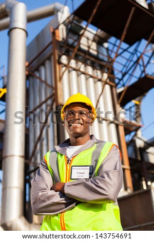 cheerful afro american oil industrial worker with arms crossed in refinery plant